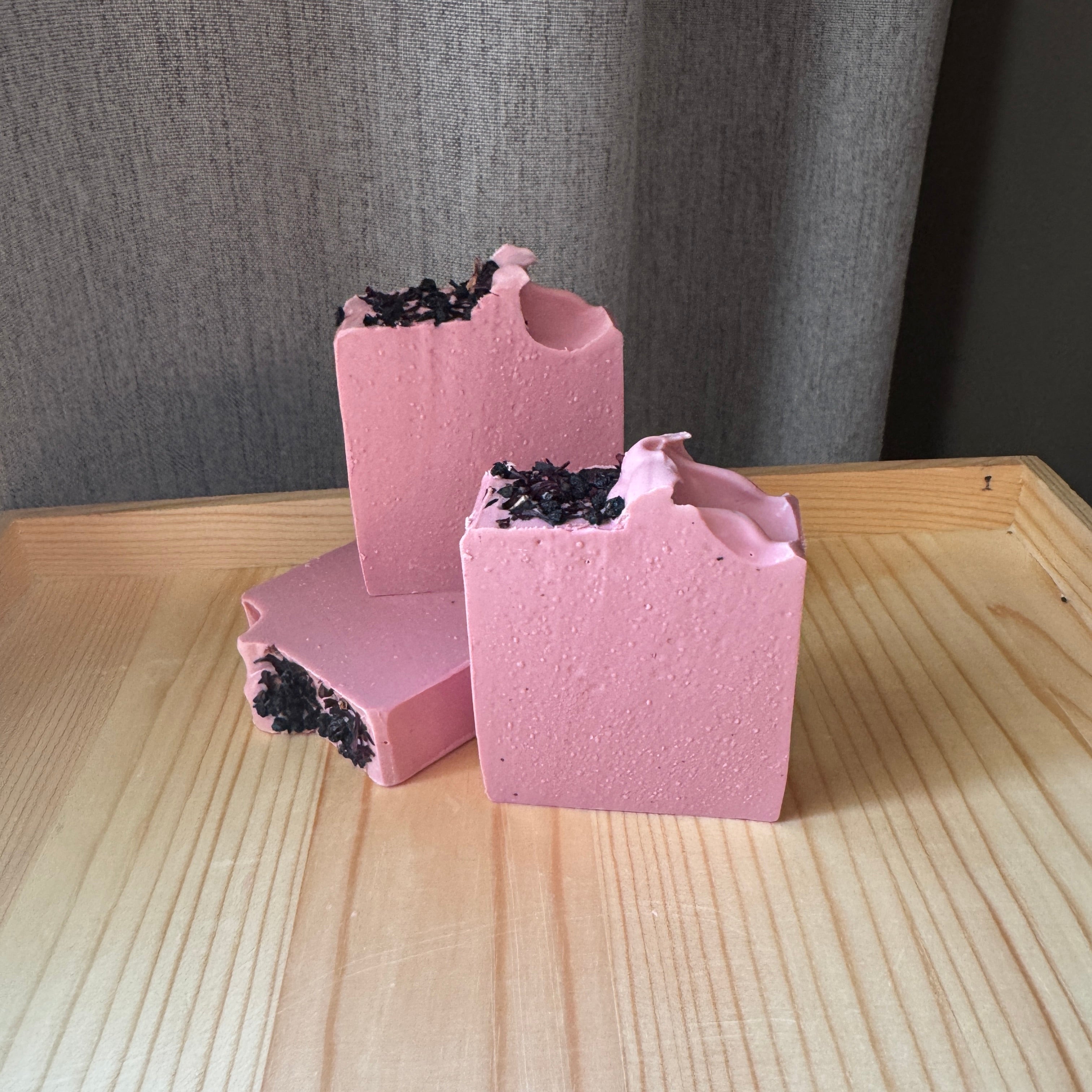 Three pink soap bars with black centers on a wooden surface.