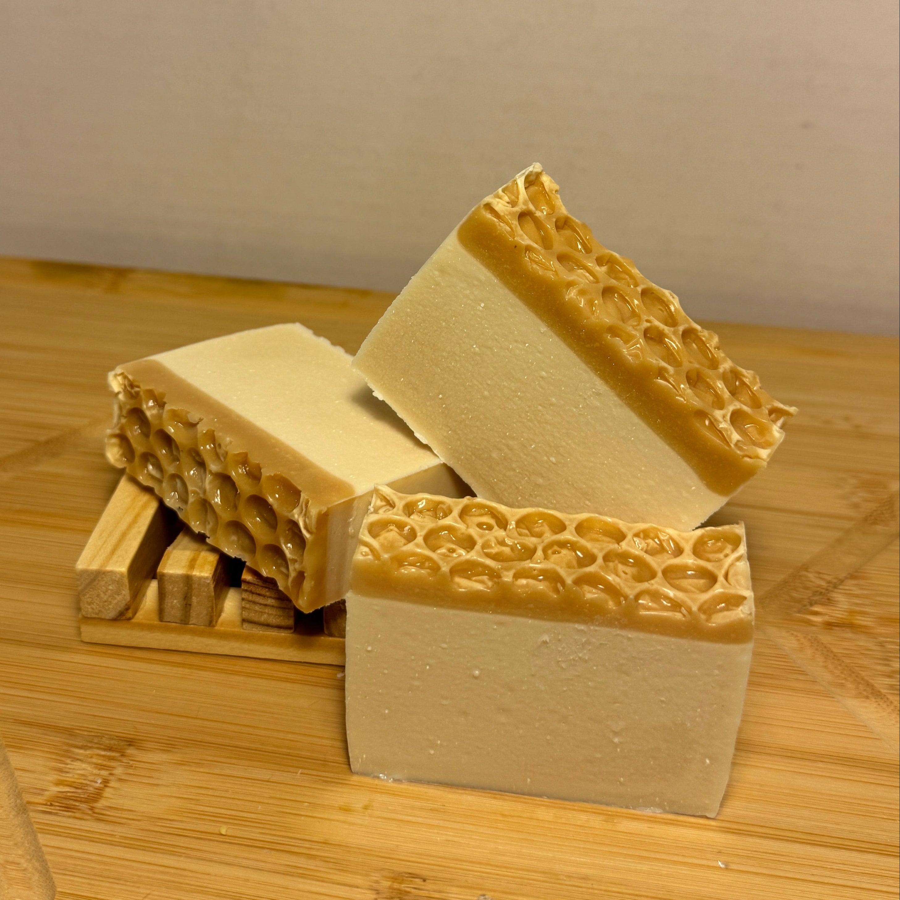 Beeswax looking blocks of soap with honeycomb pattern on top white on bottom on a wooden surface