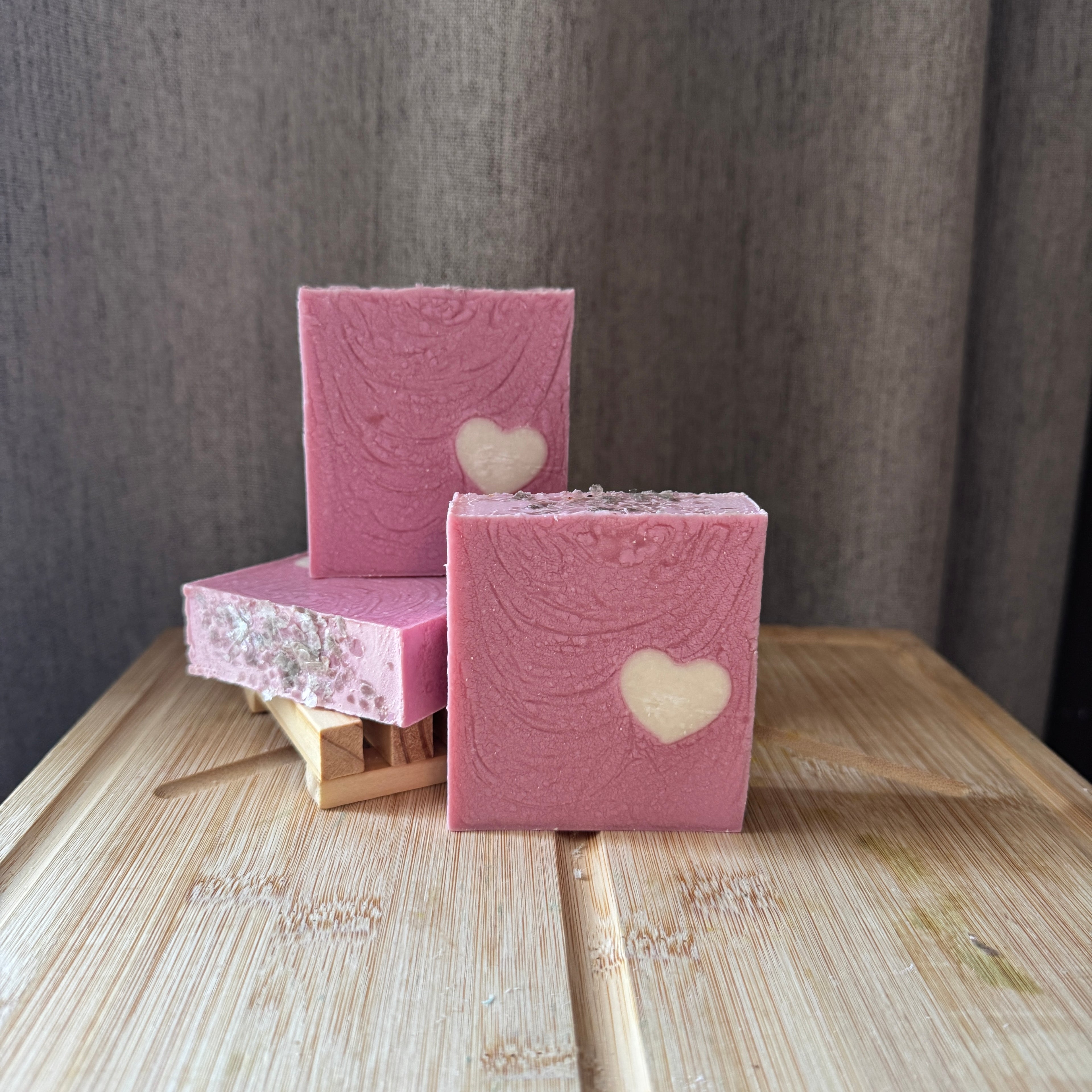 Pink soap bars with heart designs on a wooden surface against a gray background