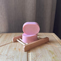 Pink soap on a wooden soap dish against a neutral background