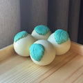 3 light yellow balls of soap topped with a green soap leaf.