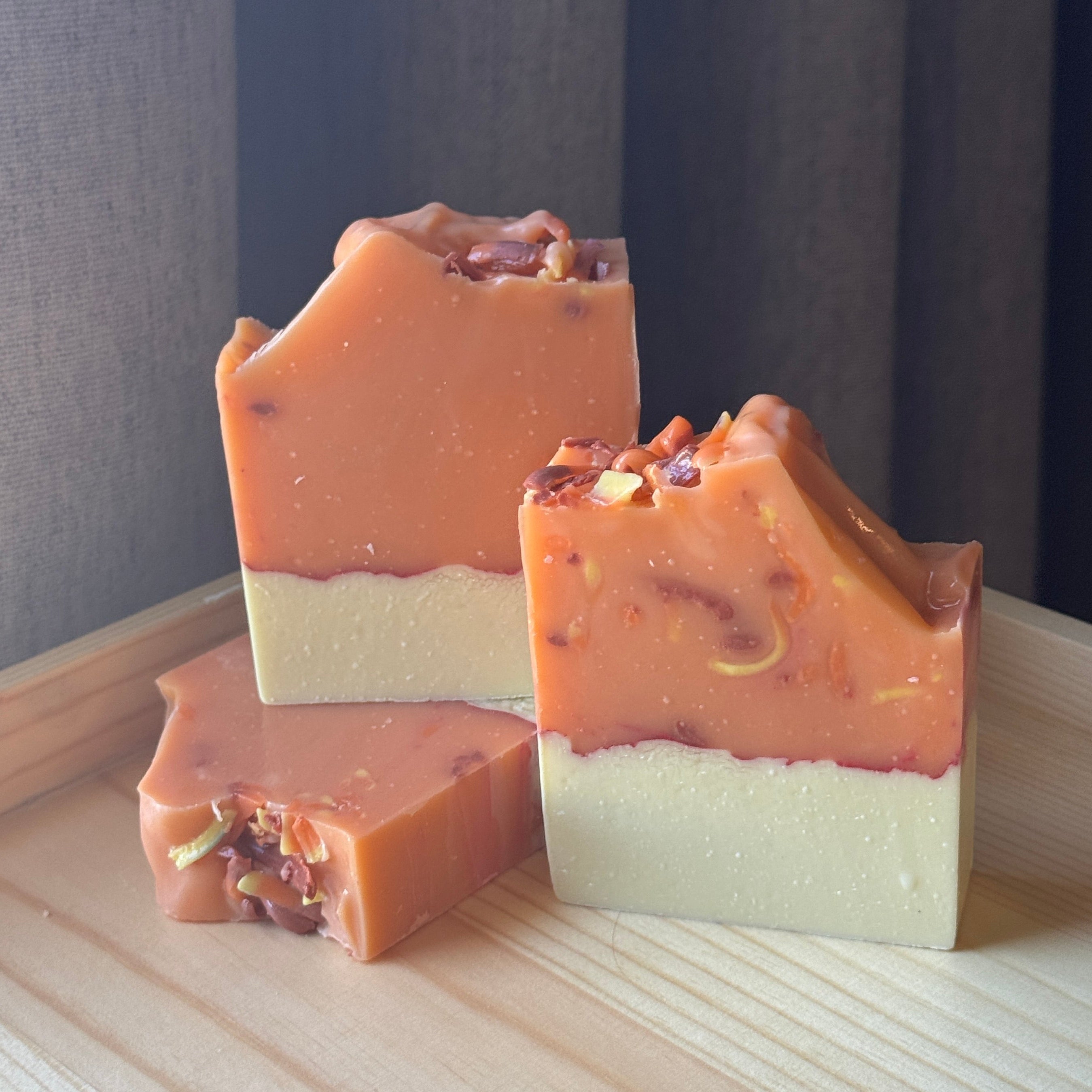 Three orange and yellow layered soap bars on a wooden surface with a neutral background