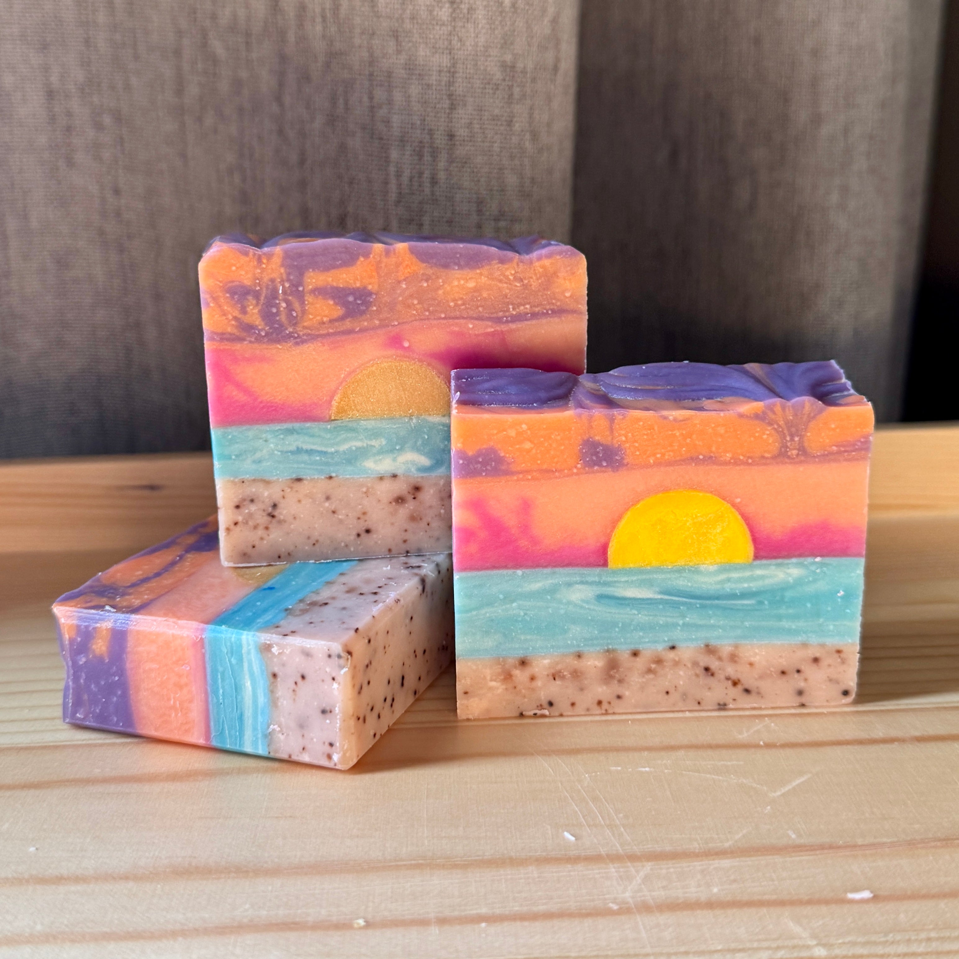 Three colorful soap bars with sunset design on a wooden surface