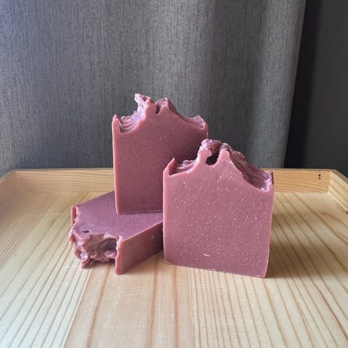 Three bars of pink soap on a wooden surface with a gray background
