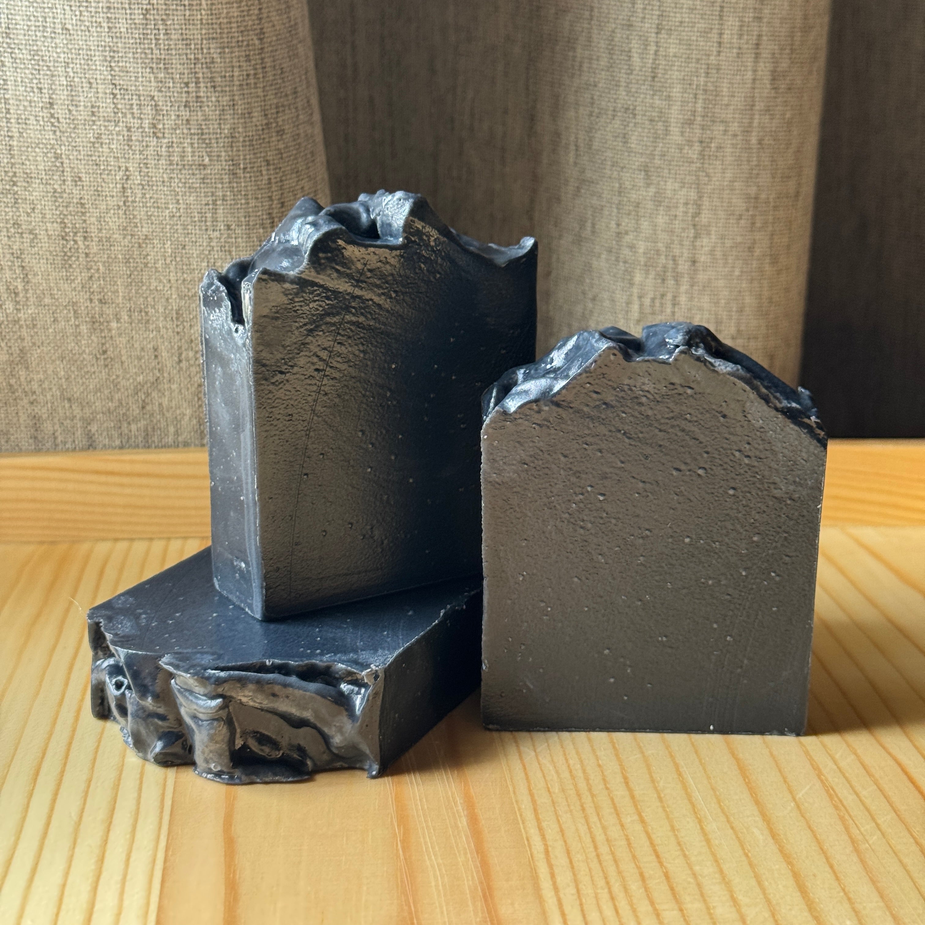 3 black handmade soap blocks arranged on a wooden surface