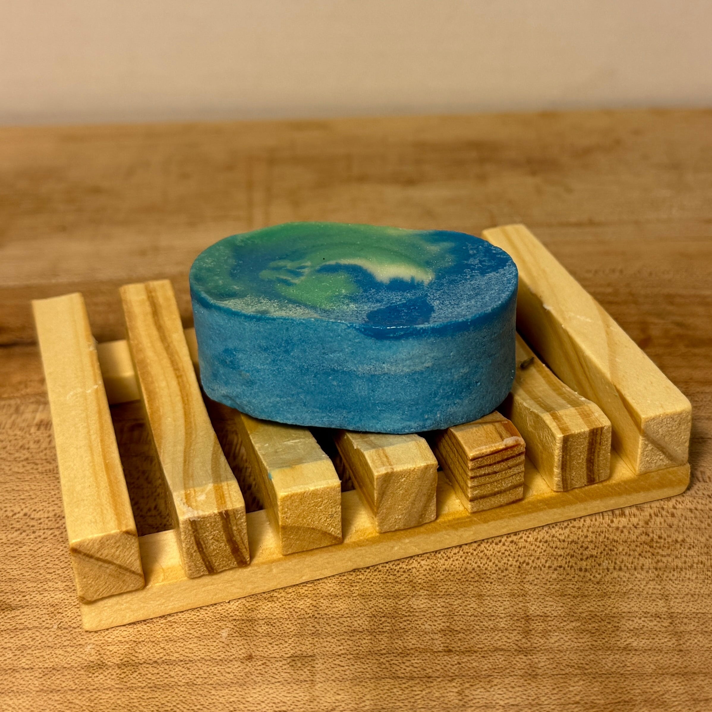 Blue bar of soap on a wooden soap dish on a wooden surface.