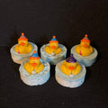 5 rubber ducks sitting on 5 round blue and white swirled soaps, wearing party hats