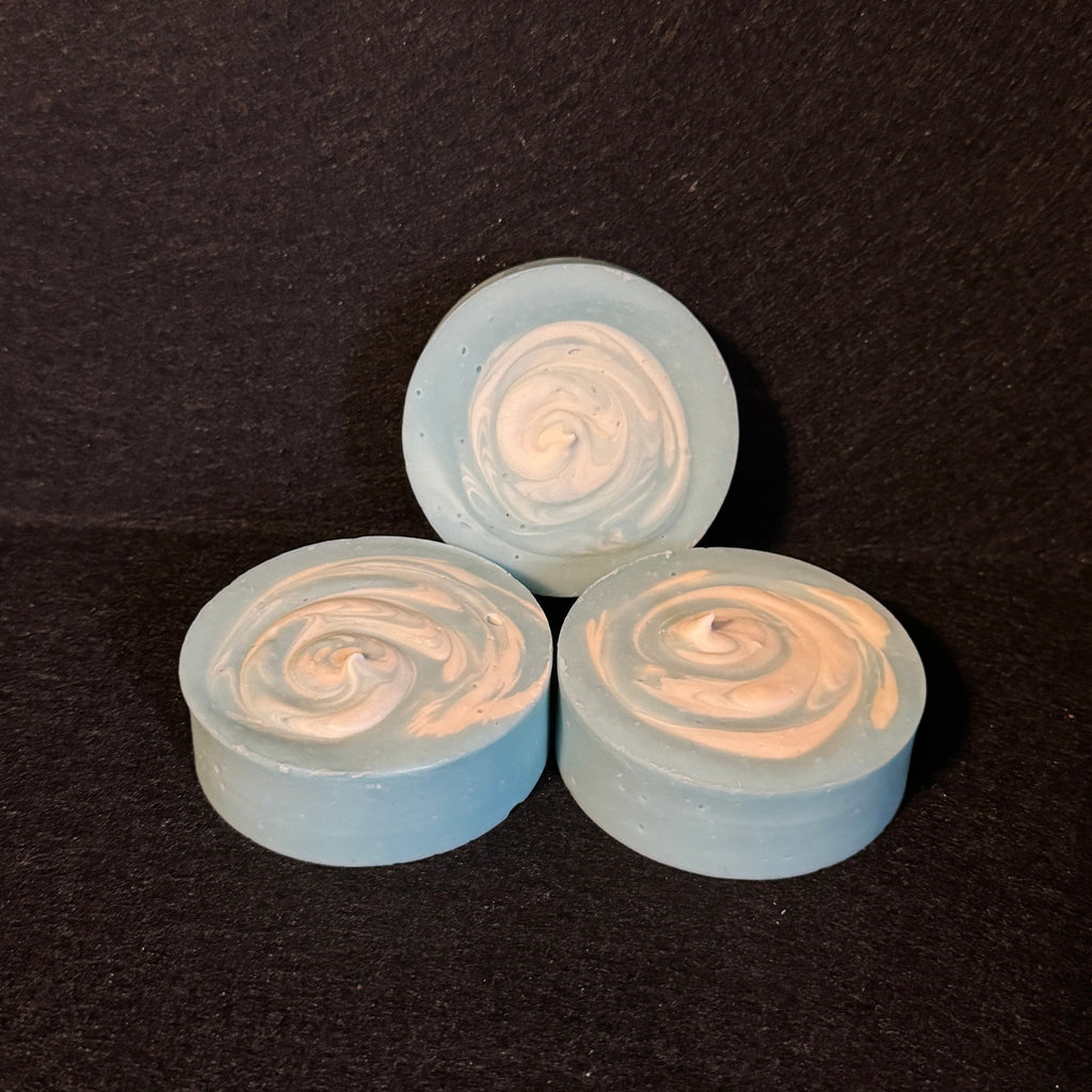 Three small round swirled items in pale blue and white, arranged on a dark textured background.
