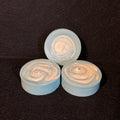 Three small round swirled items in pale blue and white, arranged on a dark textured background.