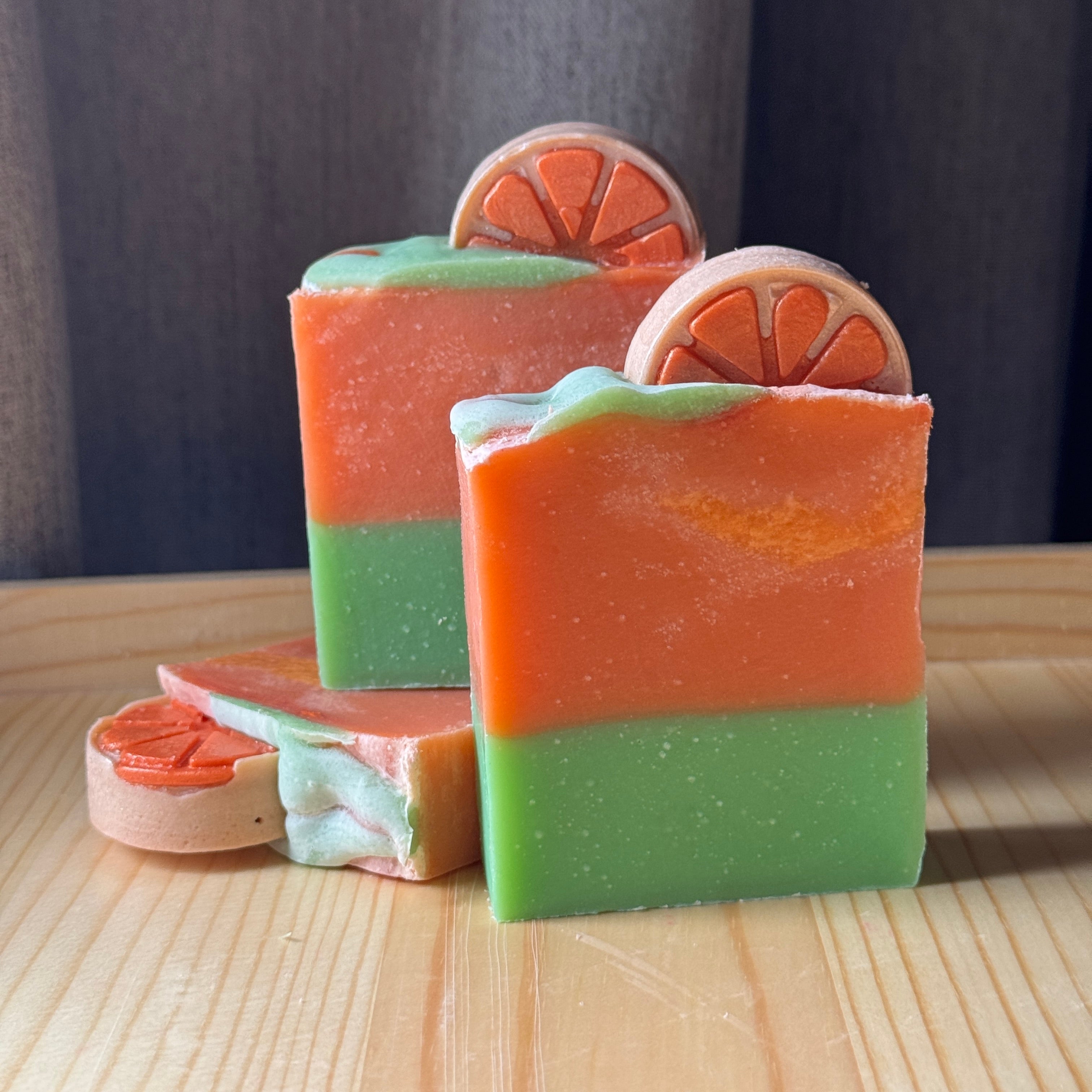 Three layered soap bars with citrus slices on a wooden surface