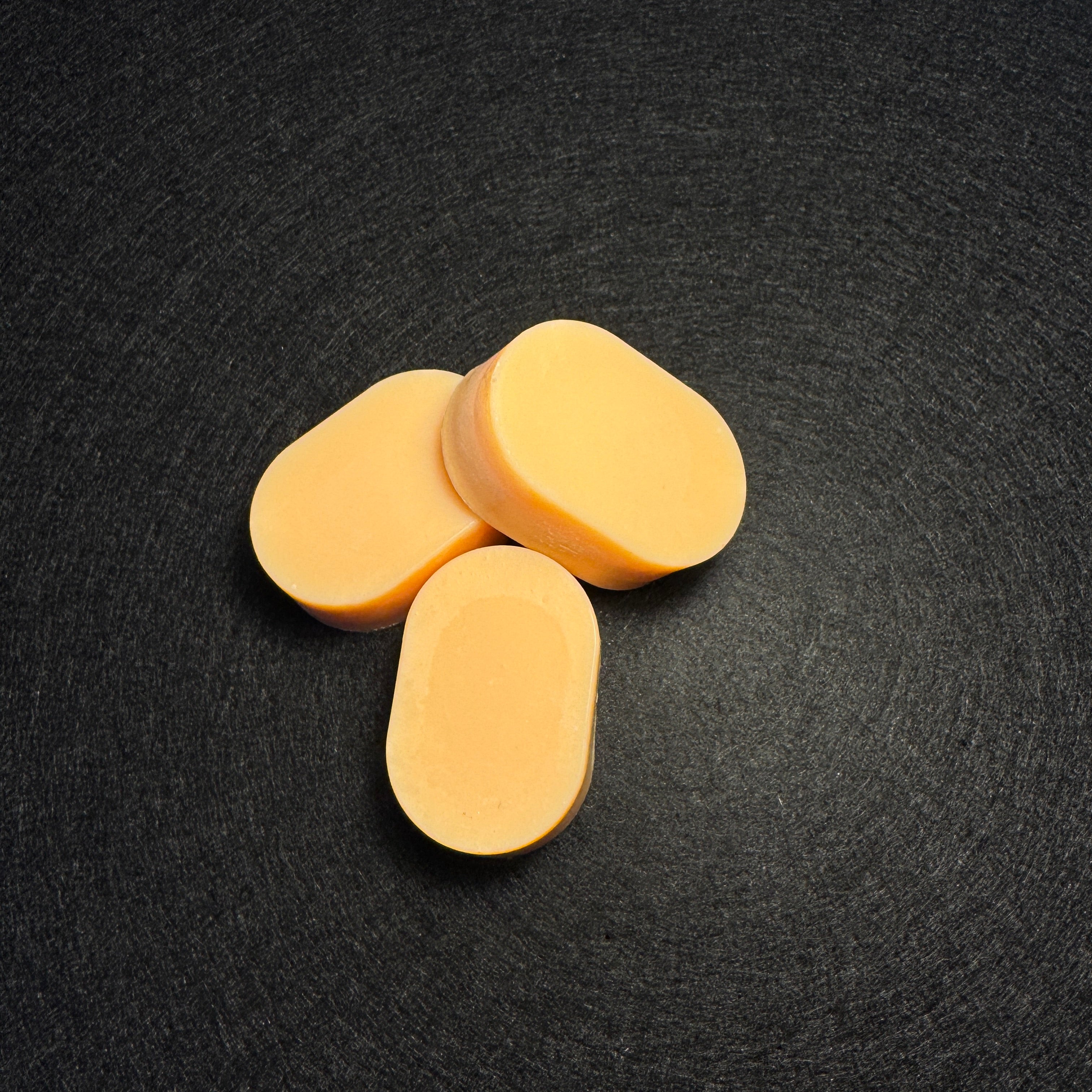 Three oval pale orange ovals arranged in a small cluster on a dark textured background.