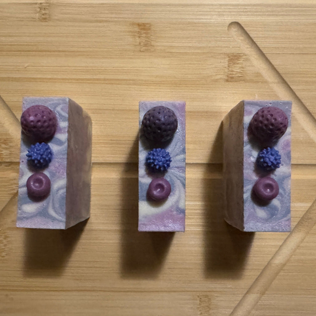 Three soap bars with berries on a wooden cutting board