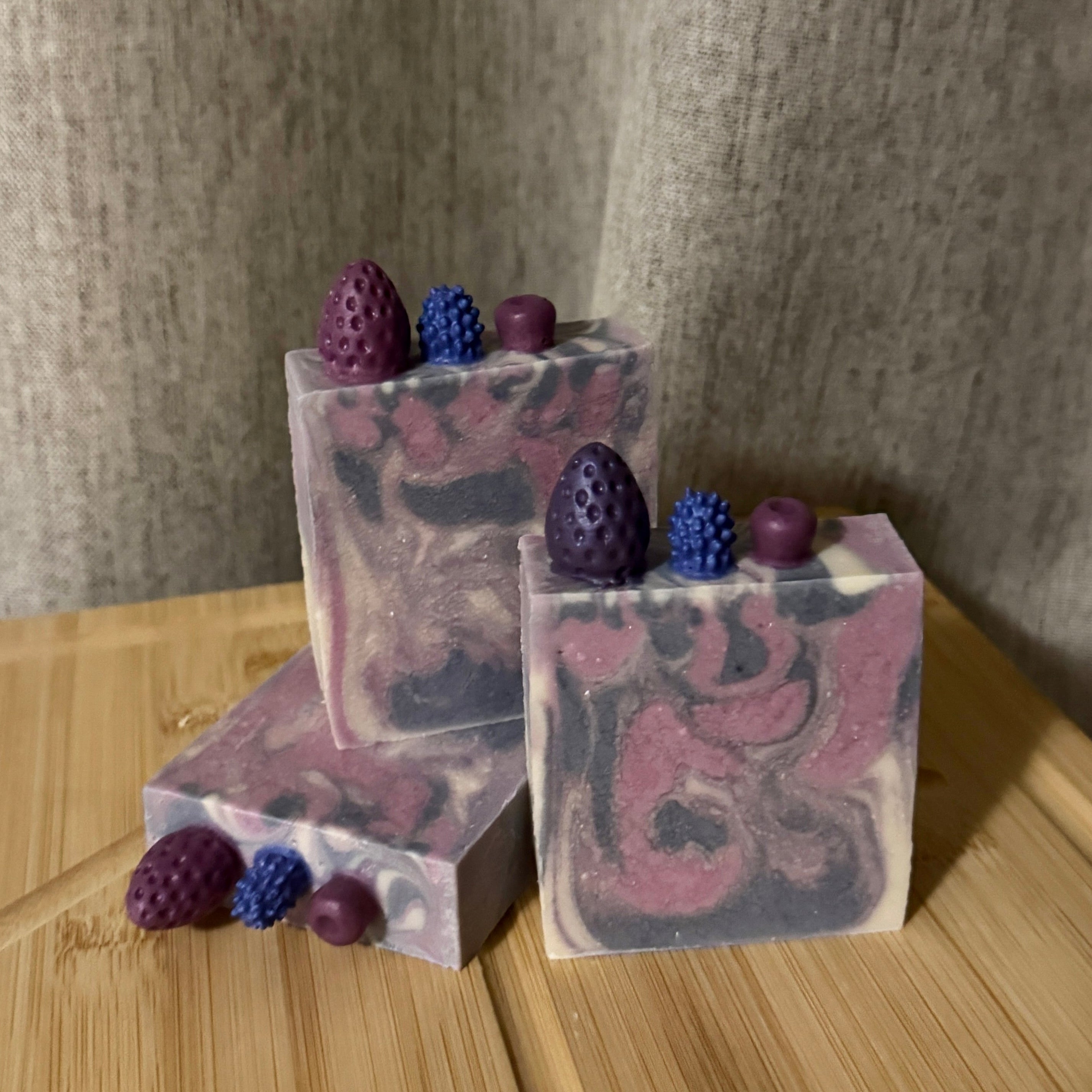 Three soap bars with embedded berries on a wooden surface
