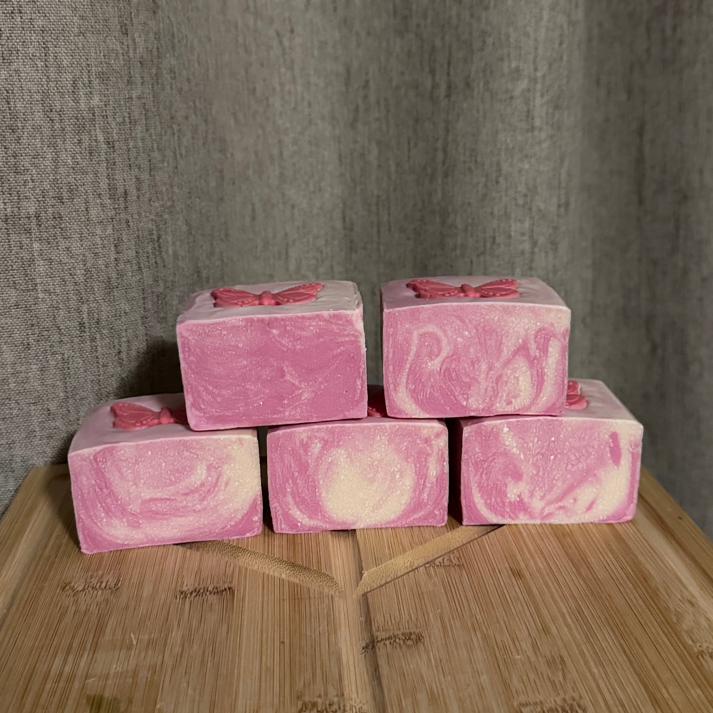 Pink marbled soap bars with butterfly decorations on a wooden surface against a gray textured background