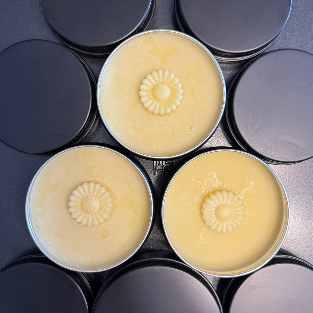 Three round containers containing lotion with a floral design on a black surface