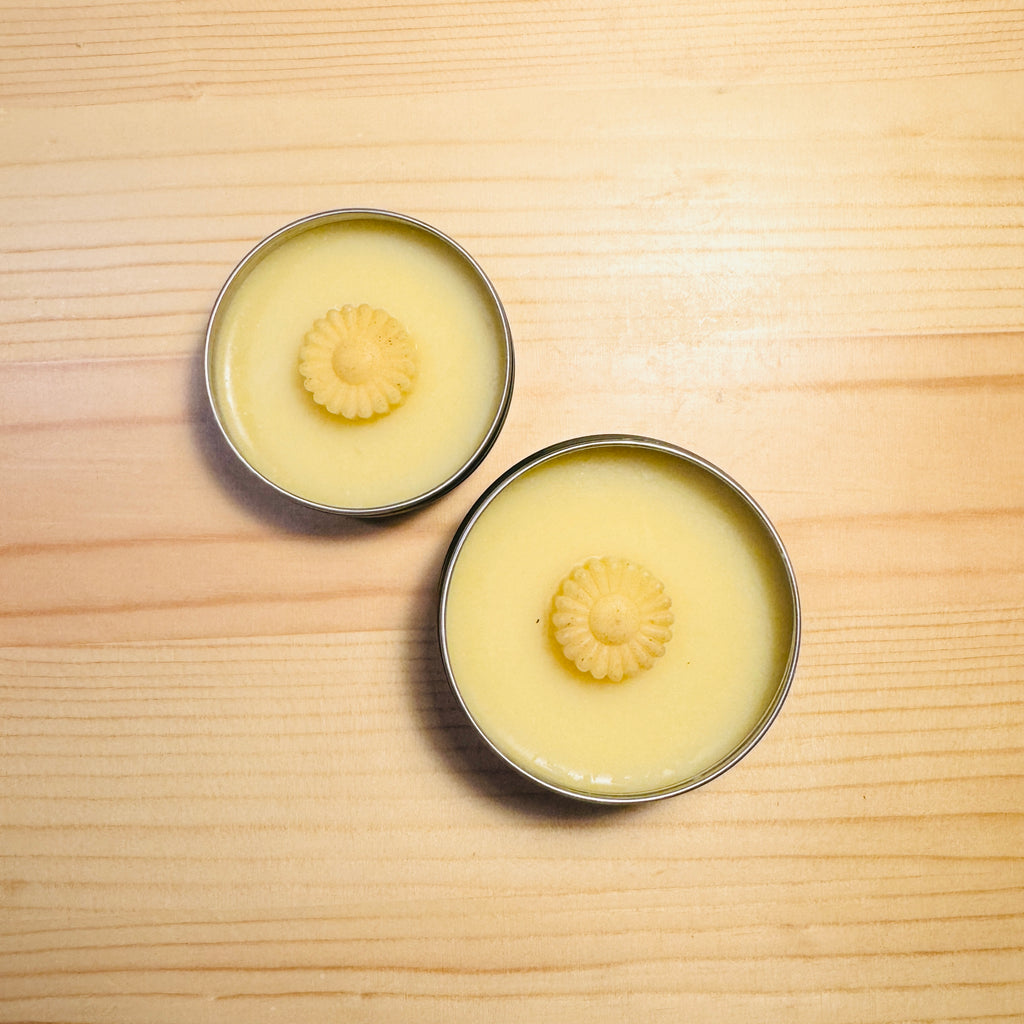 Two metal tins with a yellow substance and floral design on a wooden surface
