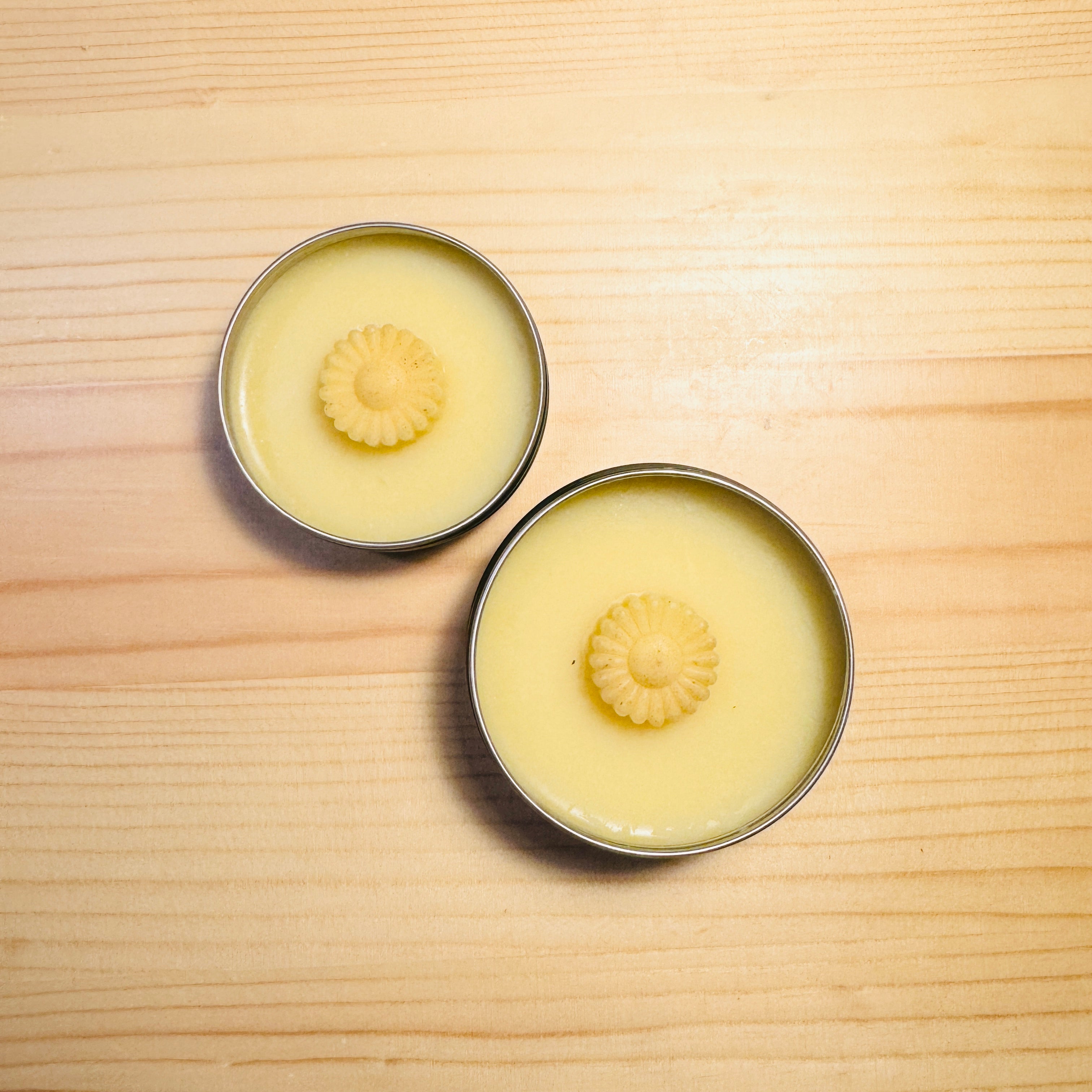 Two metal tins with a yellow substance and floral design on a wooden surface