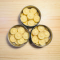 Three metal tins filled with yellow flower-shaped candies on a wooden surface.