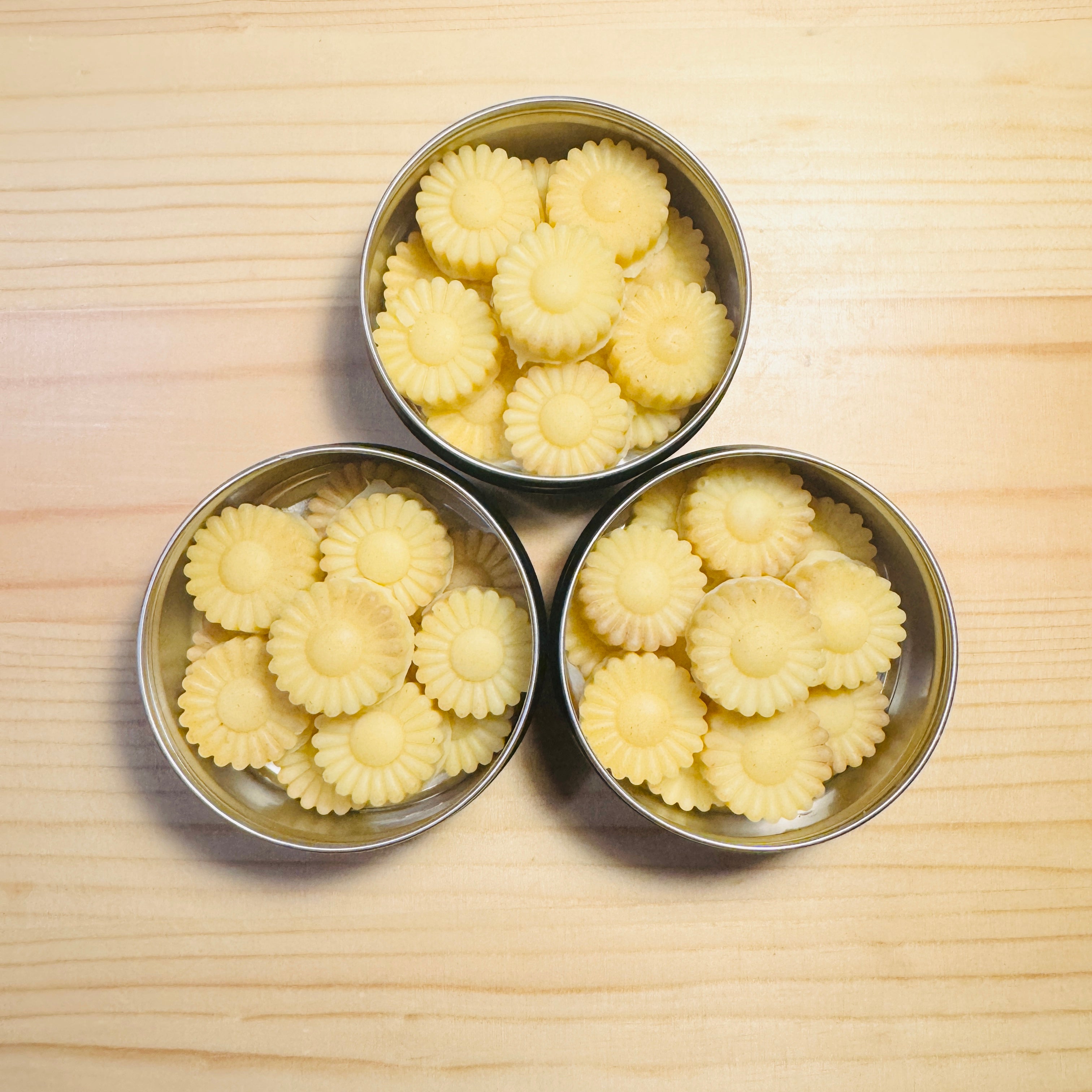 Three metal tins filled with yellow flower-shaped candies on a wooden surface.