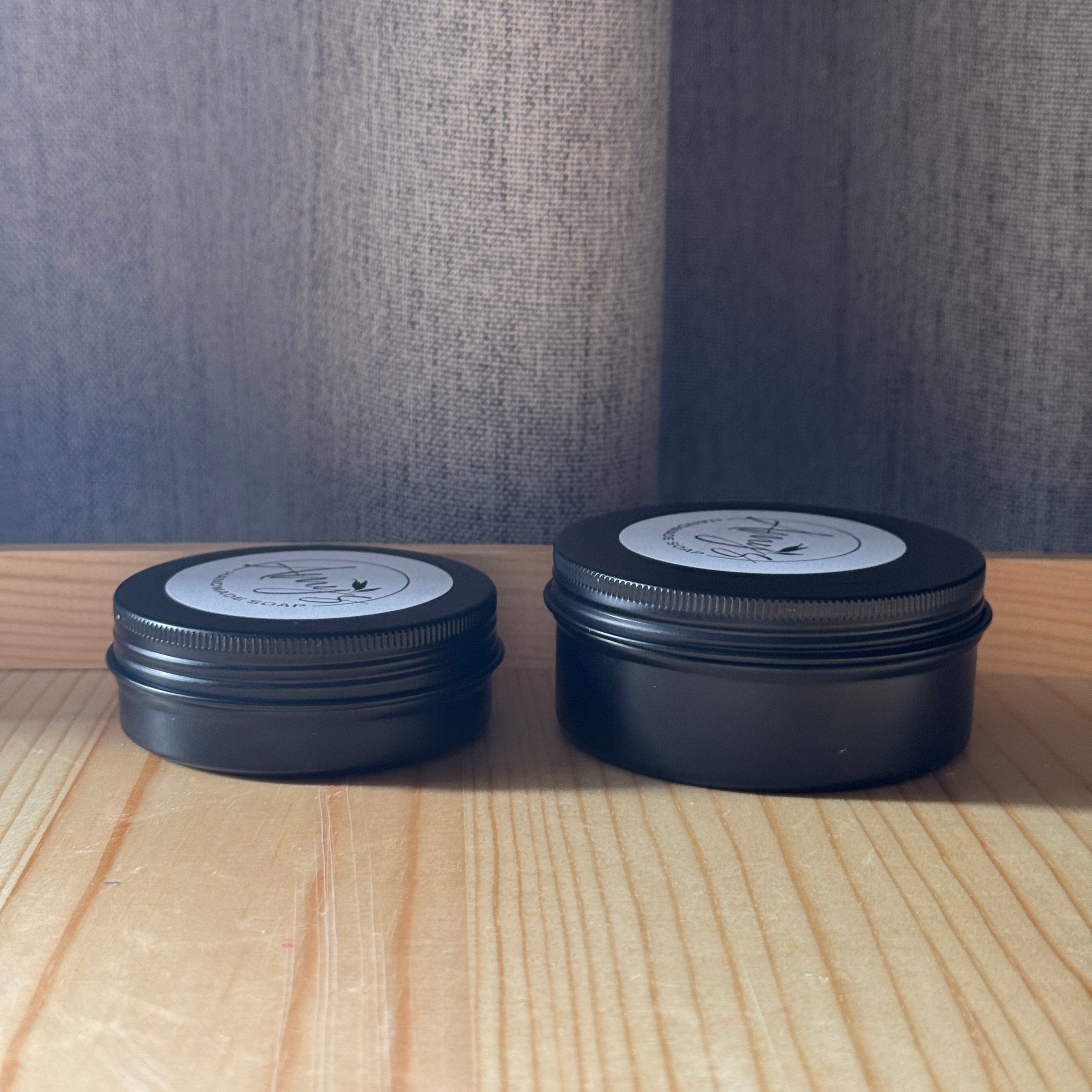 Two black metal containers with lids on a wooden surface against a textured gray wall.