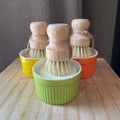 Set of three wooden-handled dish brushes in colourful ramekin on a wooden surface.