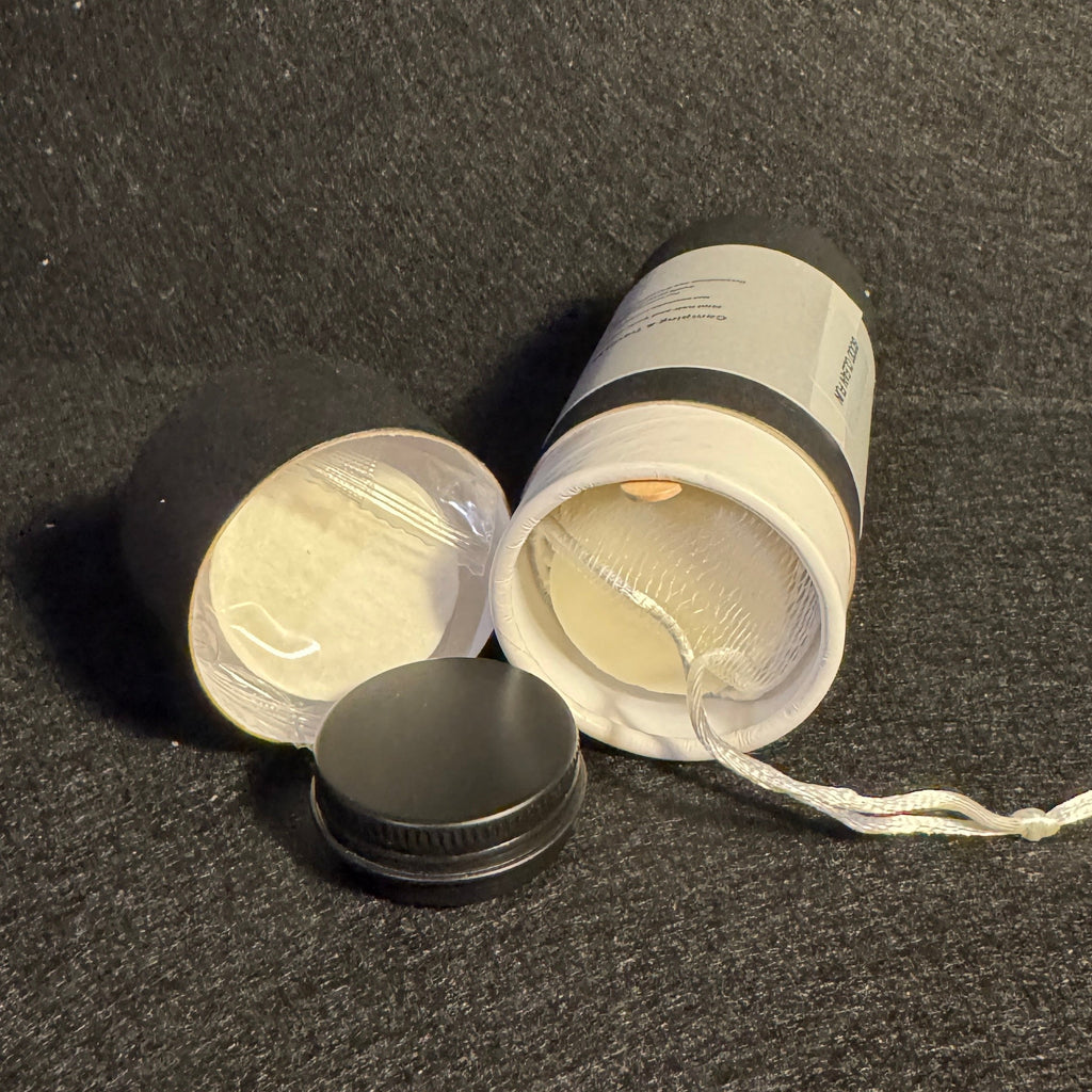 A cylindrical white jar with a black lid, shown open with its contents visible, placed on a dark textured surface.