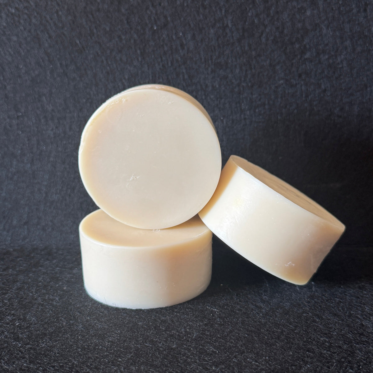 Three round, off-white solid bars stacked and leaning against each other on a dark textured background.
