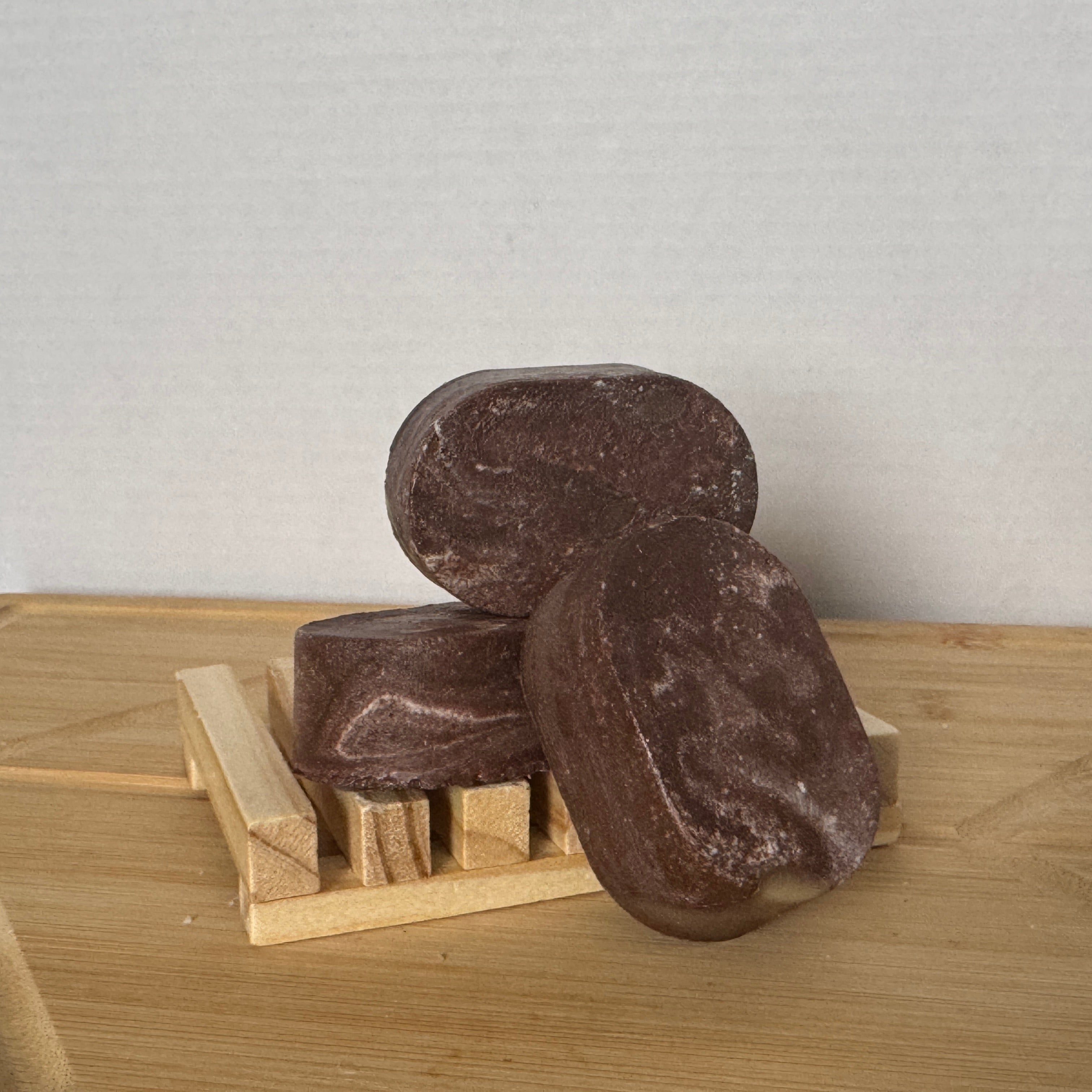 Three brown soap bars on a wooden soap dish against a light gray background