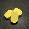 Three oval pale yellow soaps arranged on a dark textured surface.