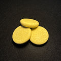 Three round, pale yellow soap bars arranged in a small pyramid on a dark textured background.
