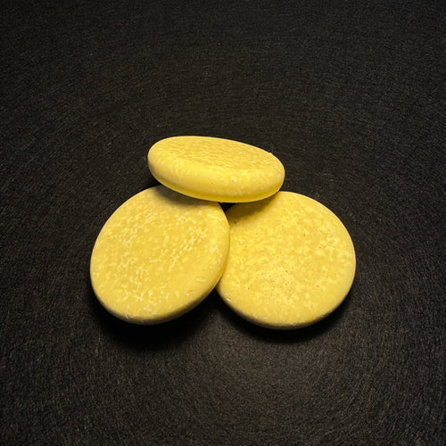 Three round, pale yellow soap bars arranged in a small pyramid on a dark textured background.