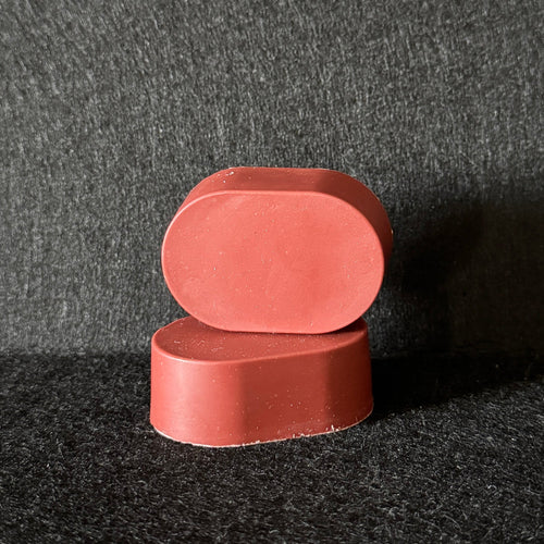 2 oval bars of red soap stacked on a black felt surface