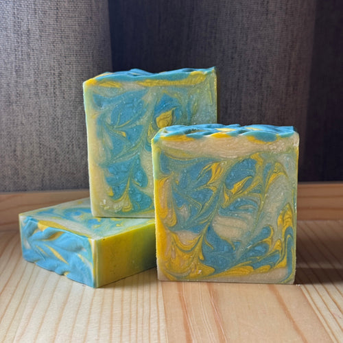 Three bars of blue and yellow marbled soap on a wooden surface with a dark fabric background.