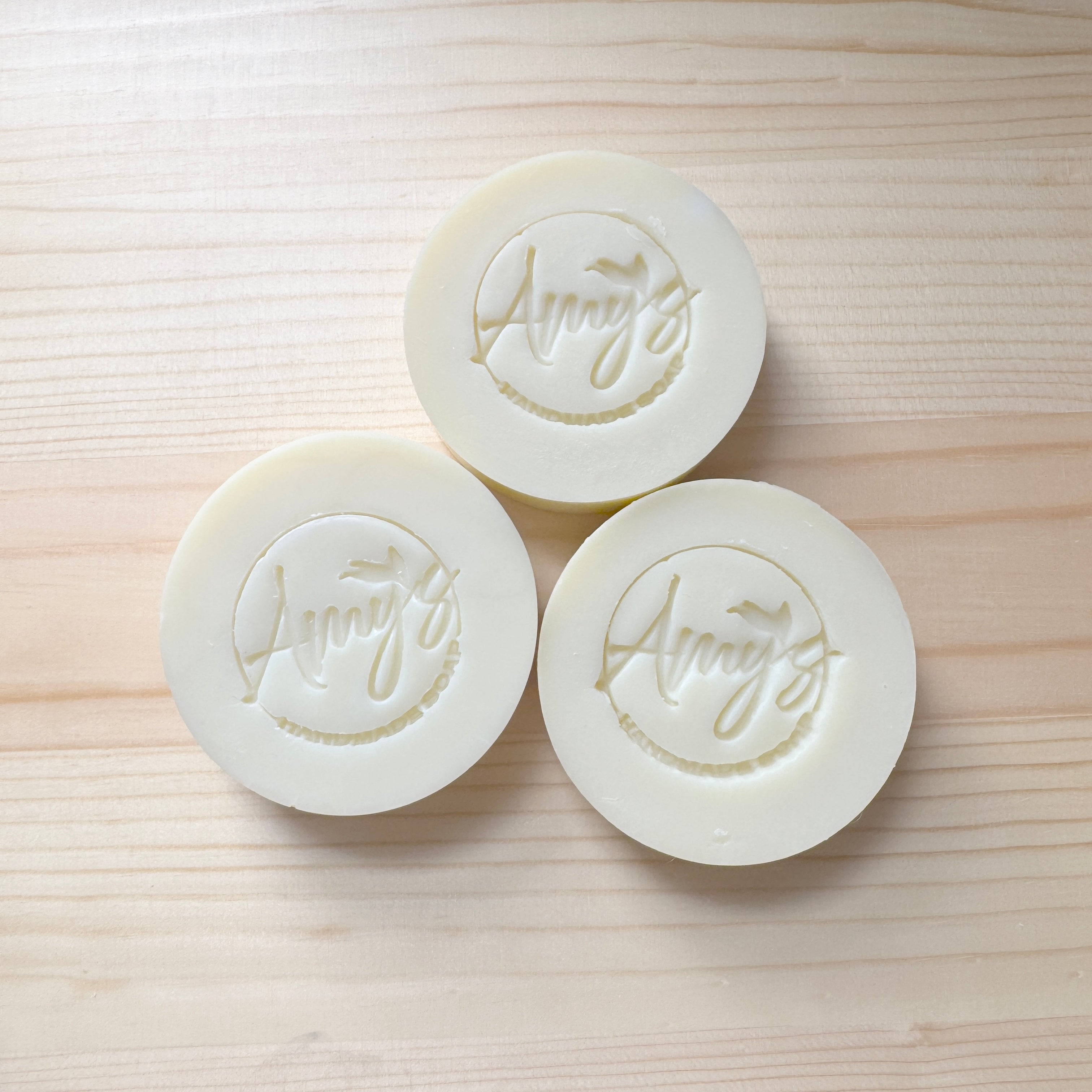 Three white soaps with 'Avery's' branding on a light wooden surface