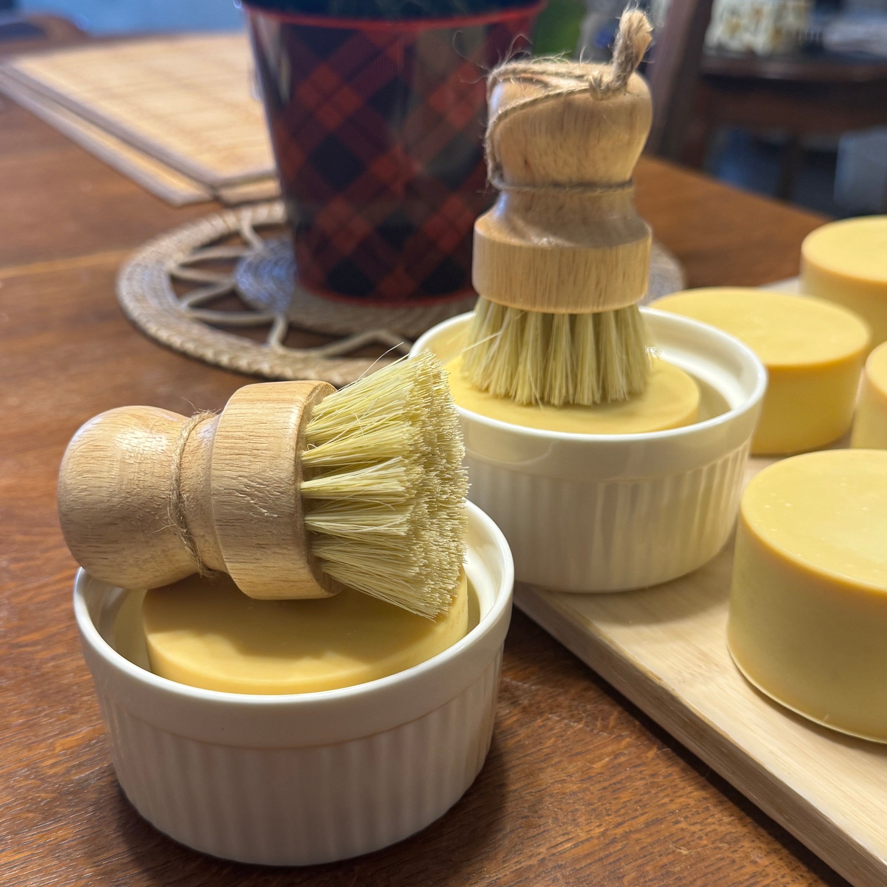 Set of wooden cleaning brushes in small white containers on a wooden surface with a plant in the background.