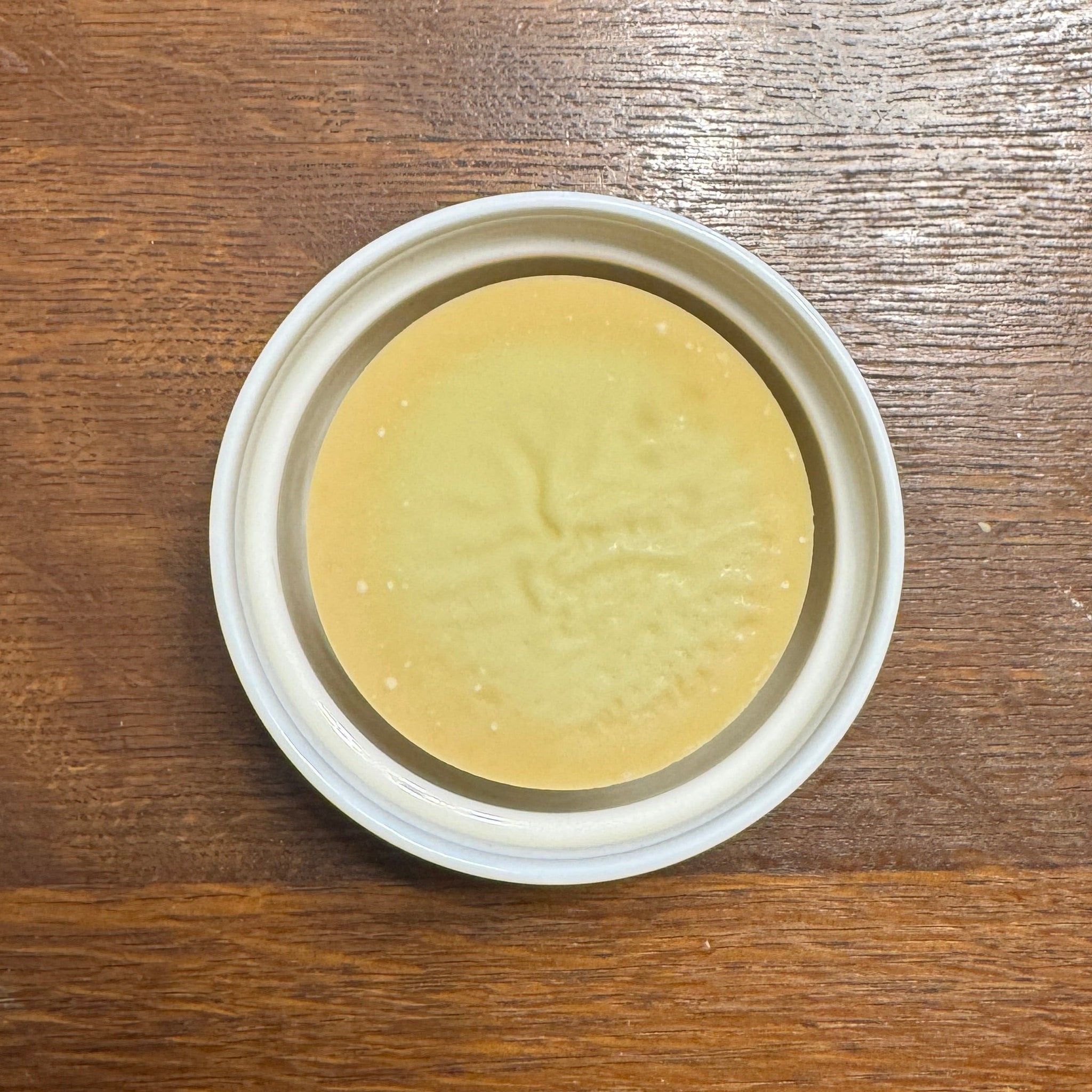 Round yellow soap in a white container on a wooden surface