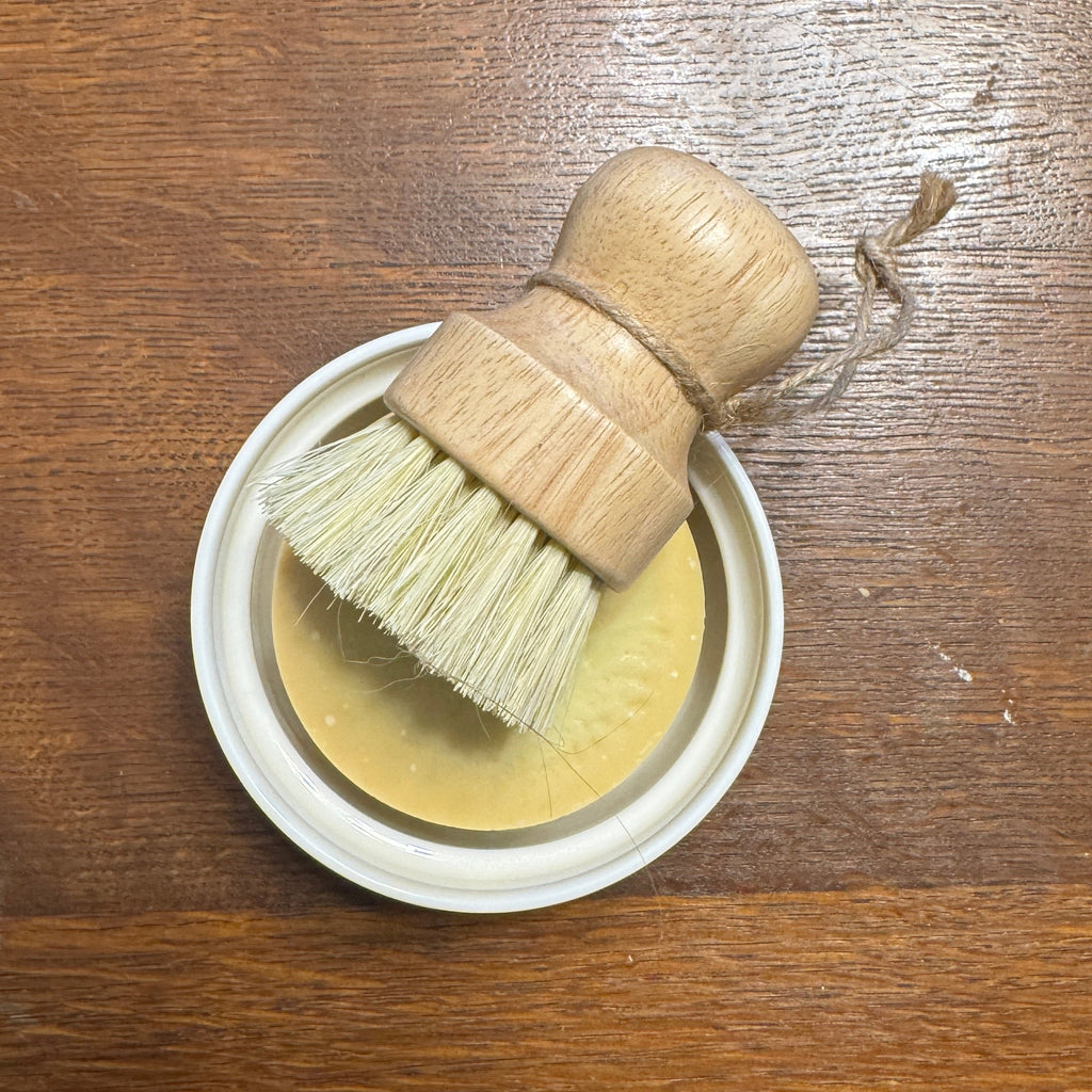 yellow solid dish soap and brush in a ramekin on a wooden surface 
