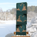 Stack of green blocks with heart shapes on a wooden stand against a snowy landscape.