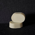 Two small oval cream-colored soap stacked on a dark textured background.