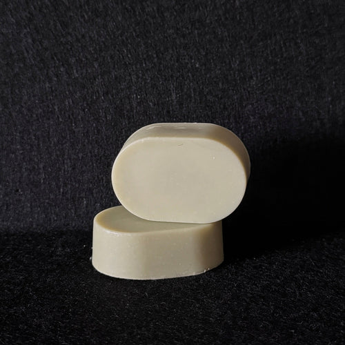 Two small oval cream-colored soap stacked on a dark textured background.