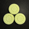 Three pale yellow-green sunflower-shaped molded pieces arranged in a triangle on a dark textured background.