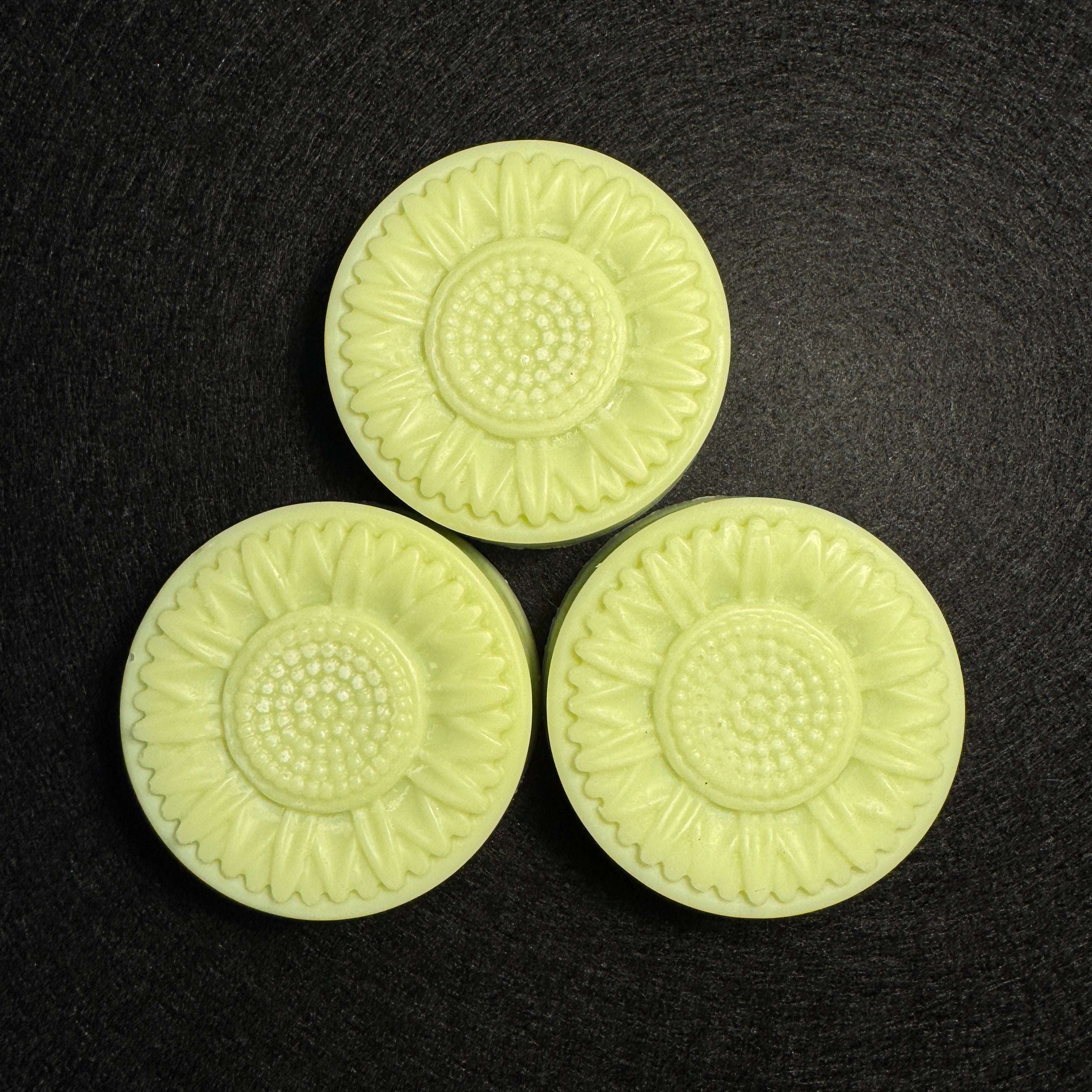Three pale yellow-green sunflower-shaped molded pieces arranged in a triangle on a dark textured background.