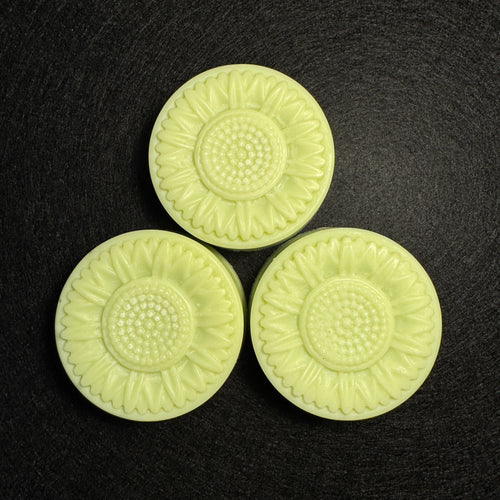 Three pale yellow-green sunflower-shaped molded pieces arranged in a triangle on a dark textured background.