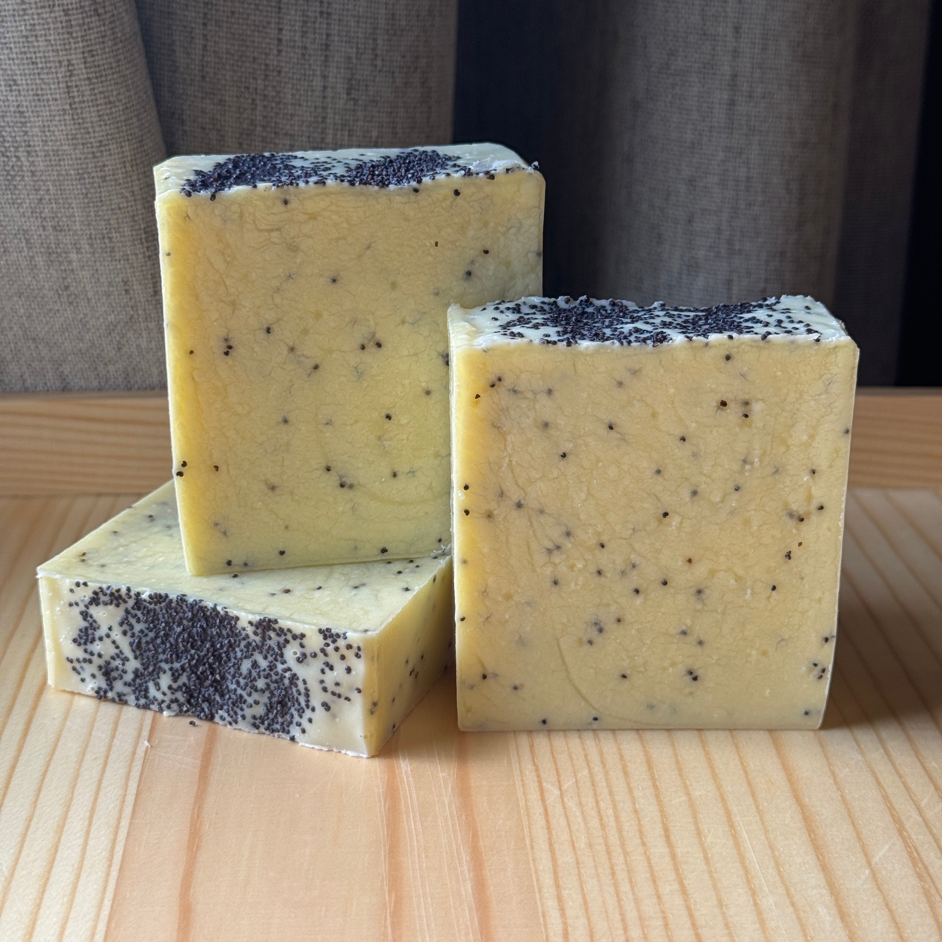 3 light yellow soaps sprinkled with poppyseeds on a wooden surface