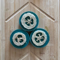 Three soaps with scrubber loofah heads on a wooden surface
