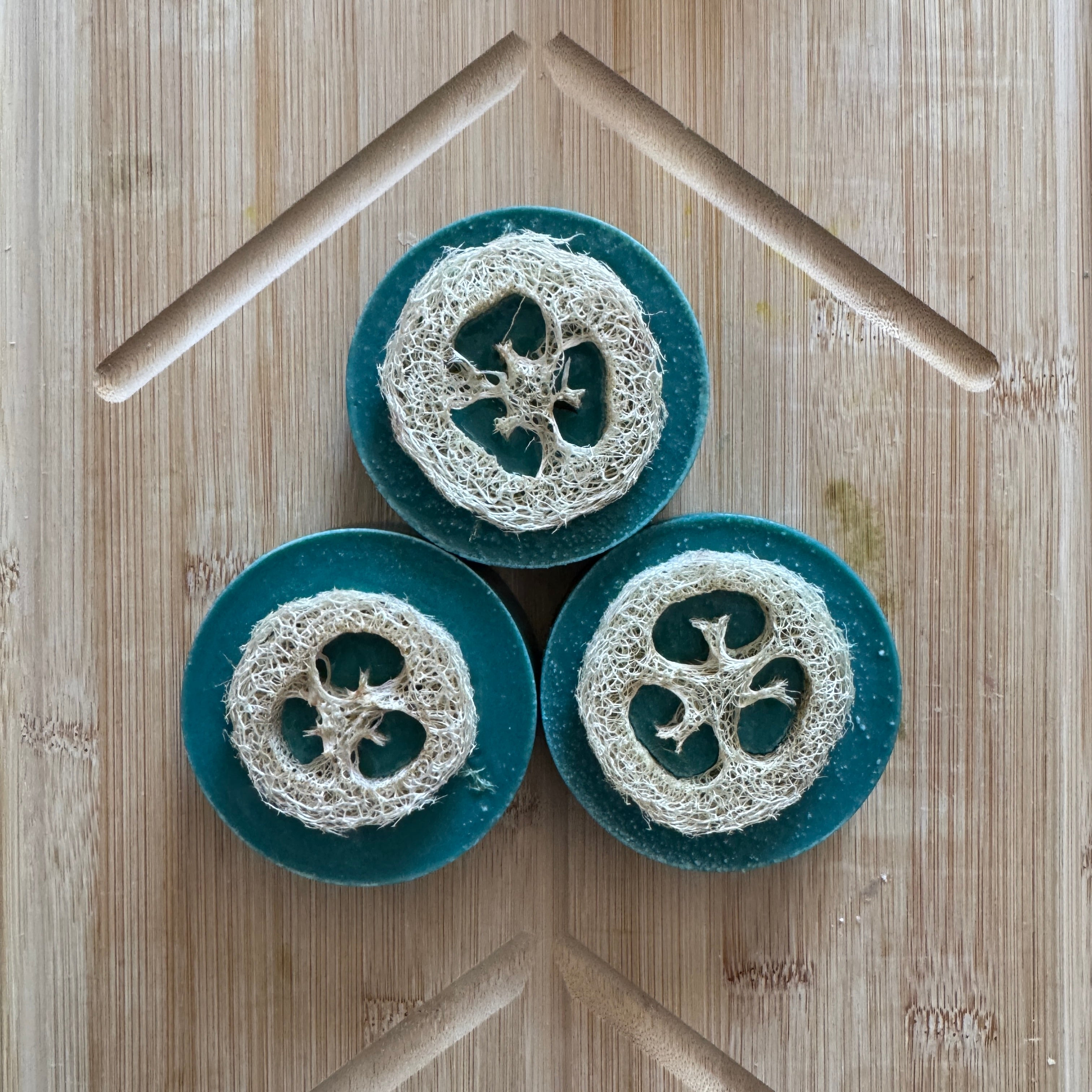 Three soaps with scrubber loofah heads on a wooden surface