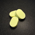 Three pale green oval-shaped soap bars arranged on a dark textured surface.