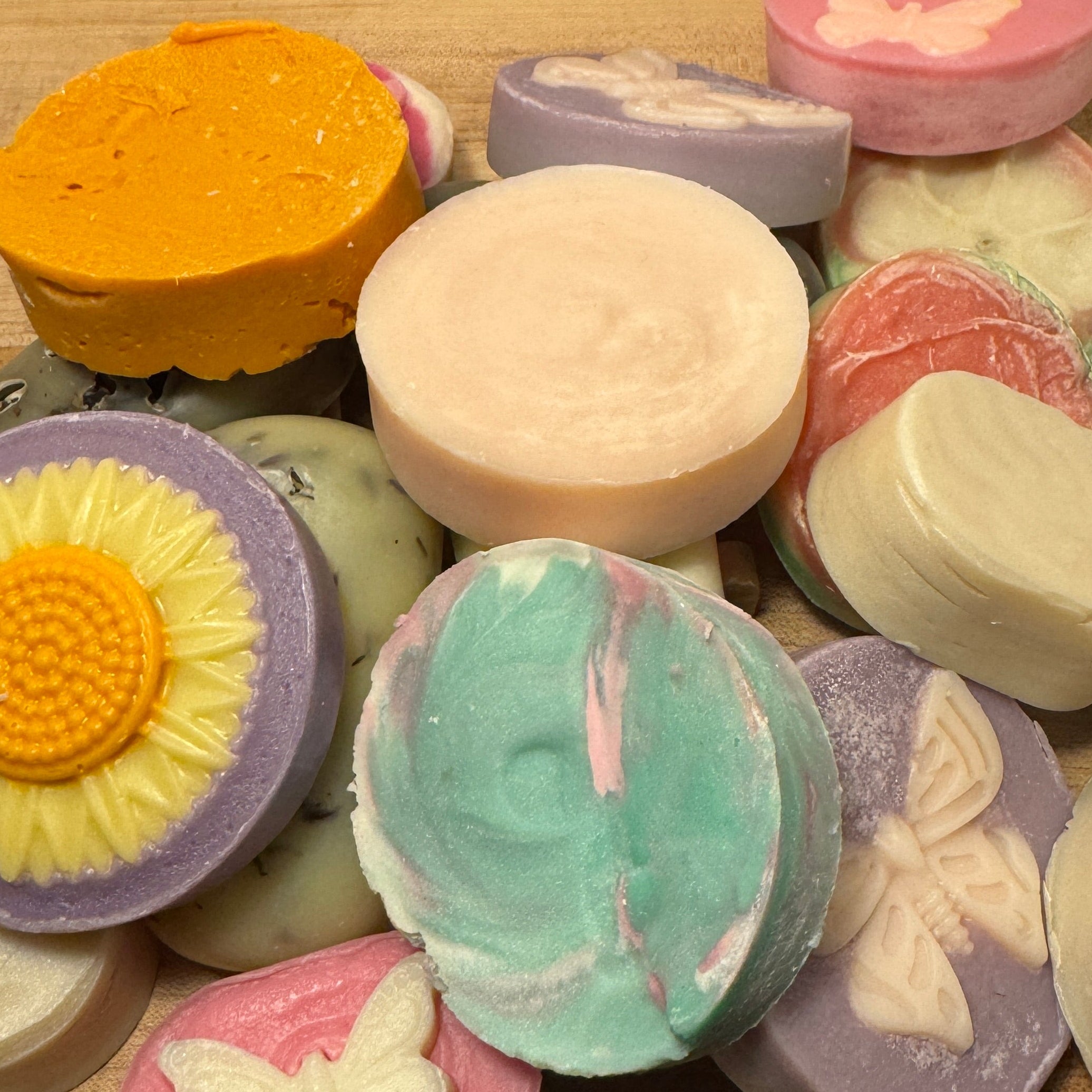 Assorted colorful soap bars with floral and butterfly designs on a wooden surface.