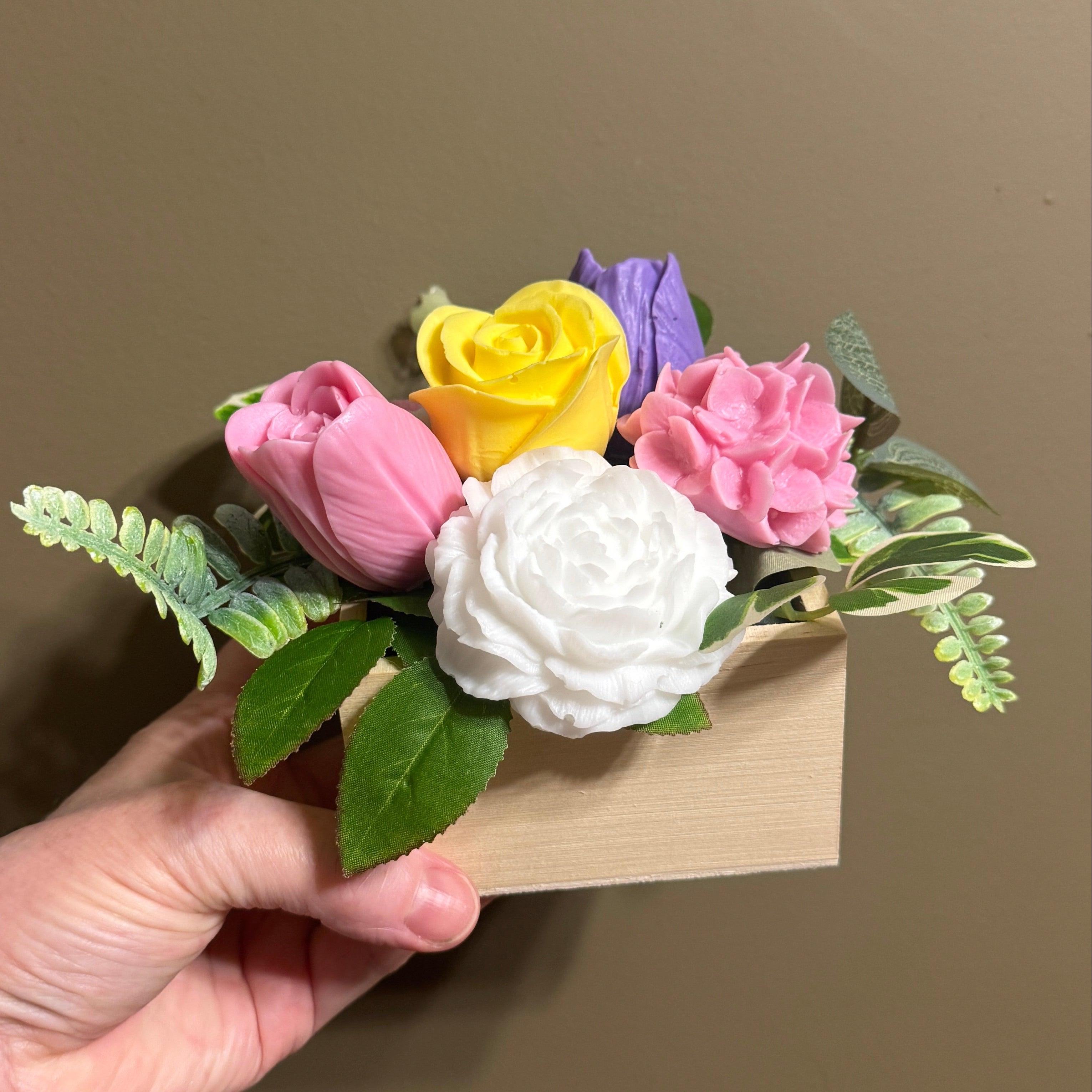 Hand holding a small bouquet of colorful artificial flowers against a plain background