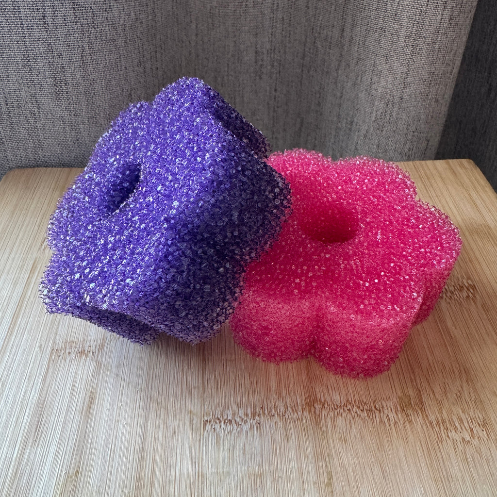 Two colorful foam sponges, one purple and one pink, on a wooden surface with a gray background.